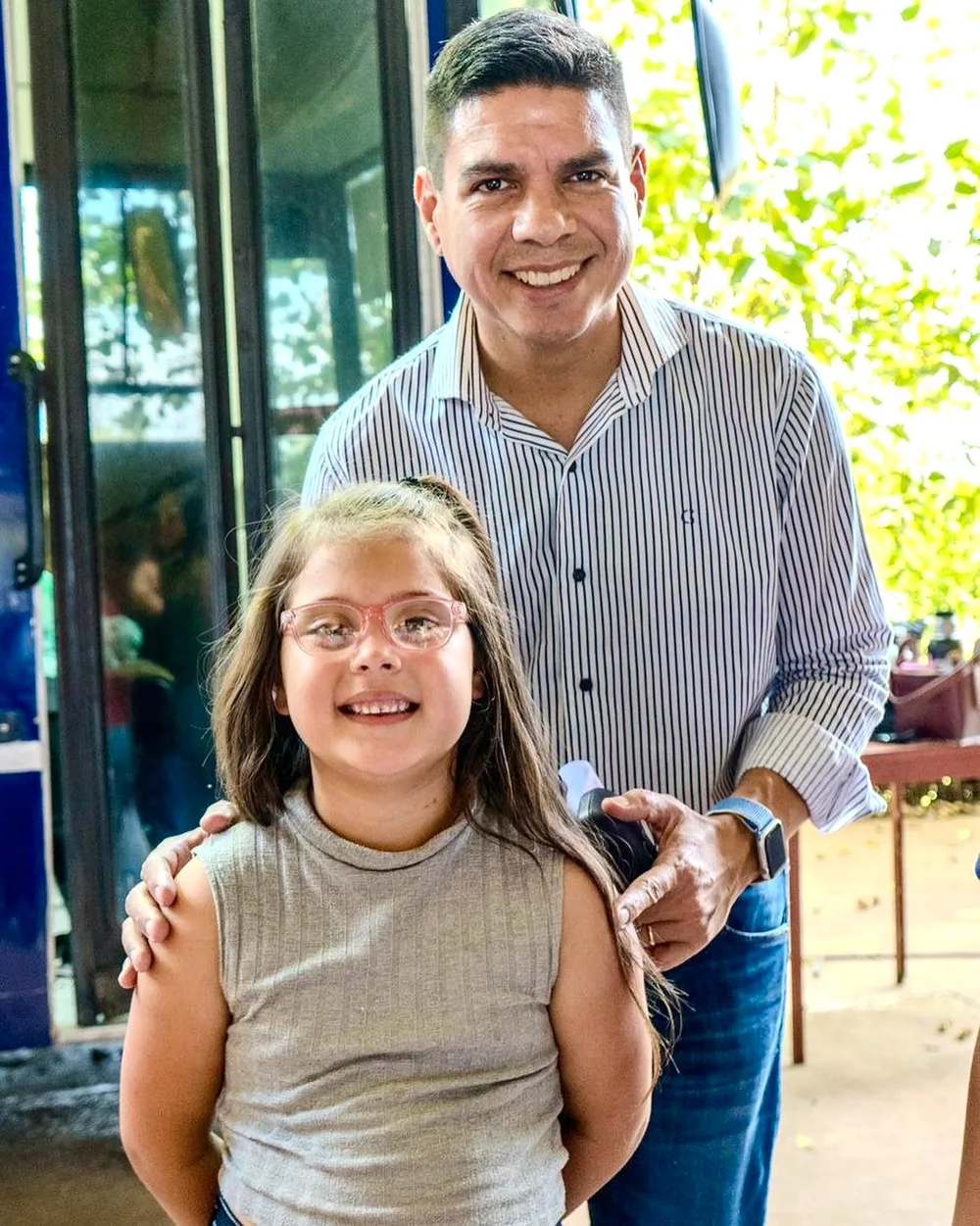 Una nena estrena sus lentes rosas nuevos y Fernando sonríe detrás de ella