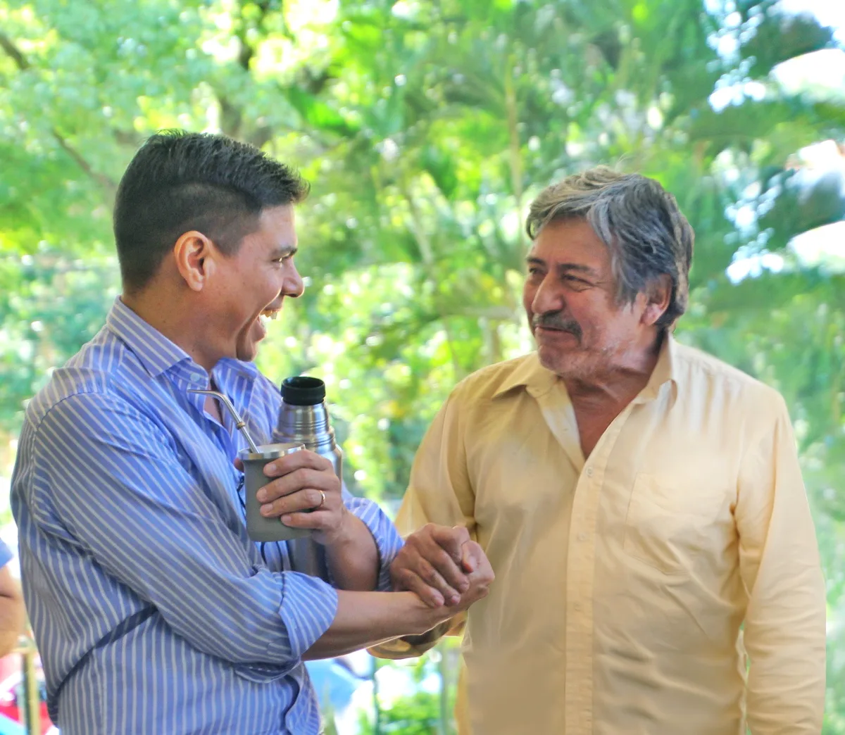Fernando, con mate y termo en la mano, se ríe junto a un señor mayor de camisa amarilla, con la selva de fondo